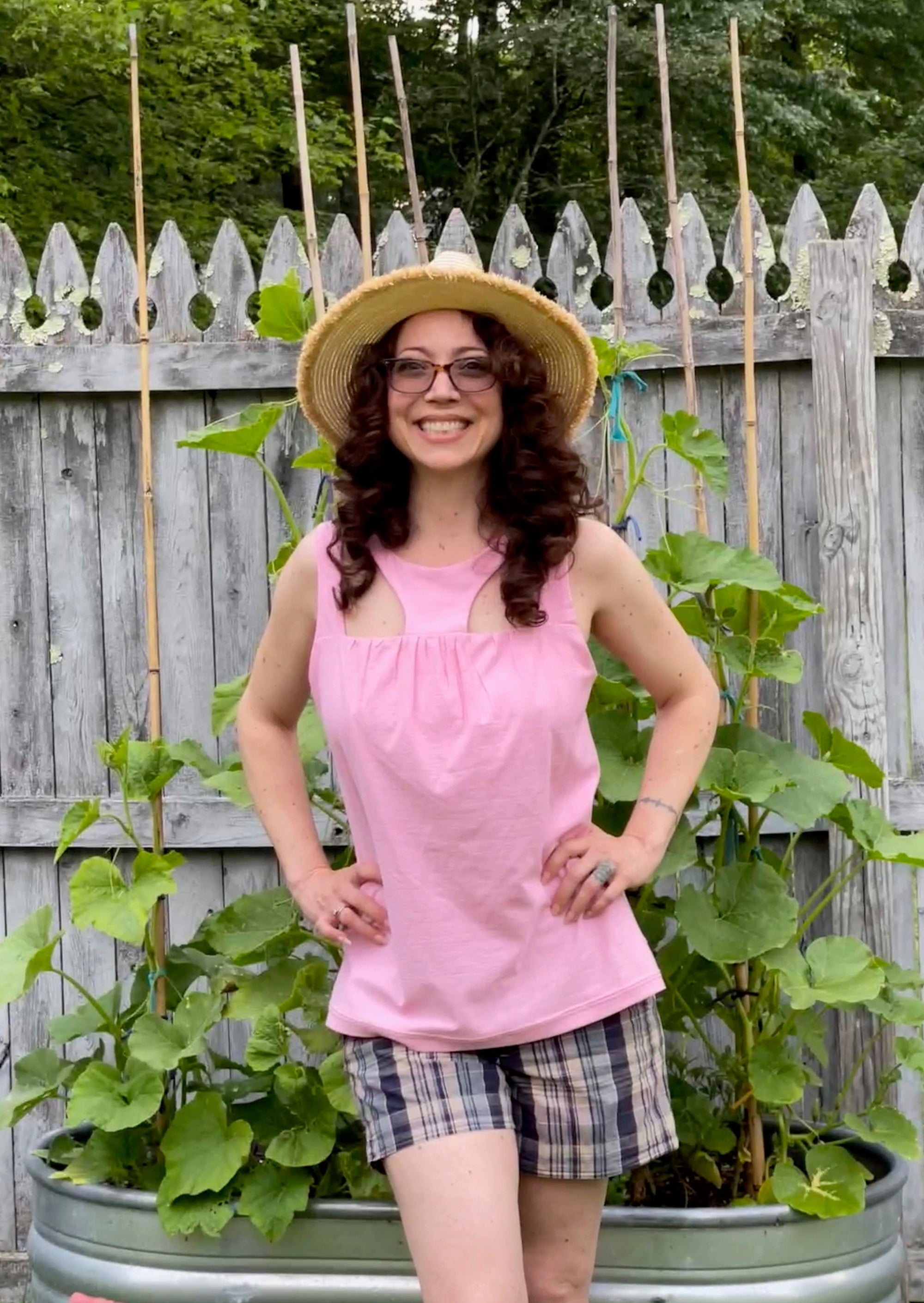 Happy woman standing  in a garden with a big hat in a cool tank top and shorts