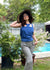 Happy woman standing by a pool in a garden with a big hat in a cool tank top and pants