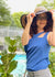 Happy woman standing by a pool in a garden with a big hat in a cool tank top and pants