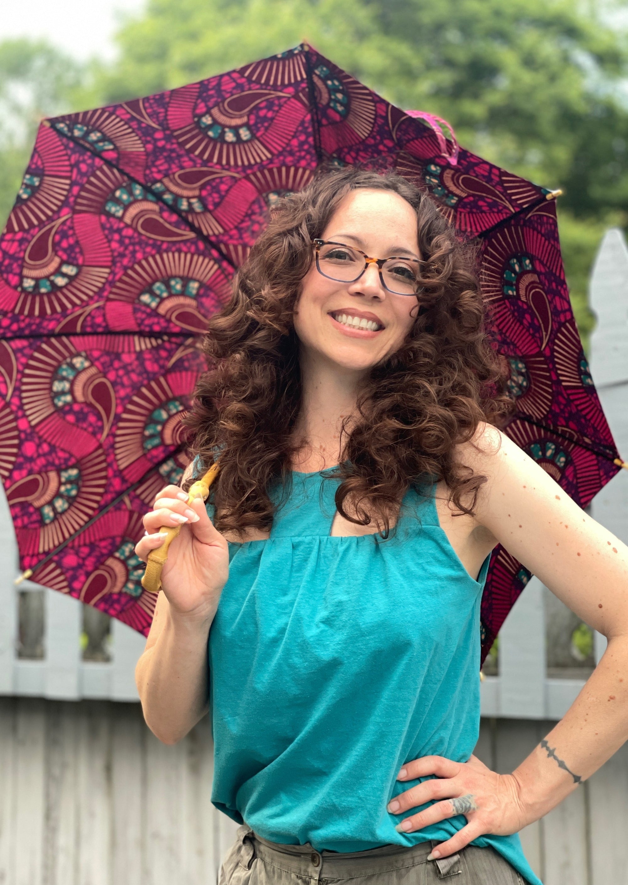 Happy woman standing by a pool in a garden  in a cool tank top holding a colorful parasol 